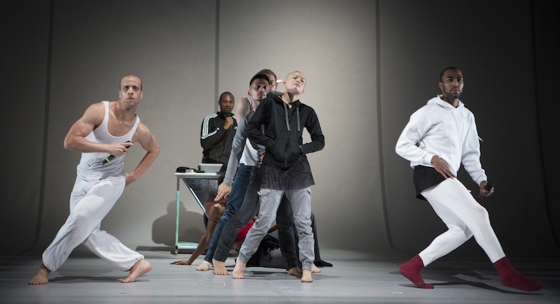 Two dancers in white with microphones. Another in a hoodie posturing in the background.